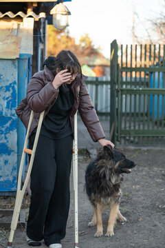 a girl on crutches walks in the yard with a dog and chickens