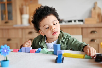 Happy little african american boy with bushy curly hair playing with colorful wooden blocks, enjoying table games playing alone at home kitchen , close up