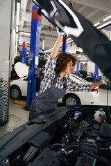 Naklejka premium Pretty auto repair shop employee lifts car hood