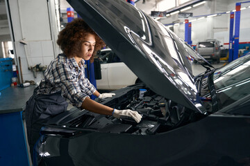 Employee of auto repair shop inspects the car under hood