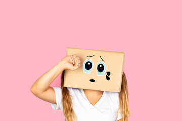 Mujer con caja de cartón en la cabeza con gesto de tristeza y con lágrimas en los ojos sobre fondo rosa liso y aislado. Vista de frente. Copy space  - obrazy, fototapety, plakaty