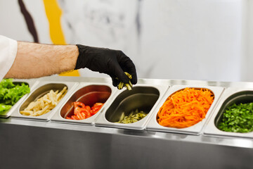a cook in rubber gloves picks up chopped vegetables for a salad