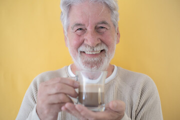 Portrait of Smiling Senior Bearded Man Holding a Glass of Coffee and Milk, Cappuccino Looking at Camera, on Yellow Background