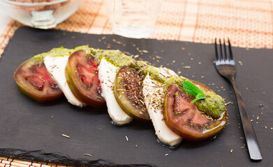 caprese salad with mozzarella, black tomatoes and pesto on black stone plate