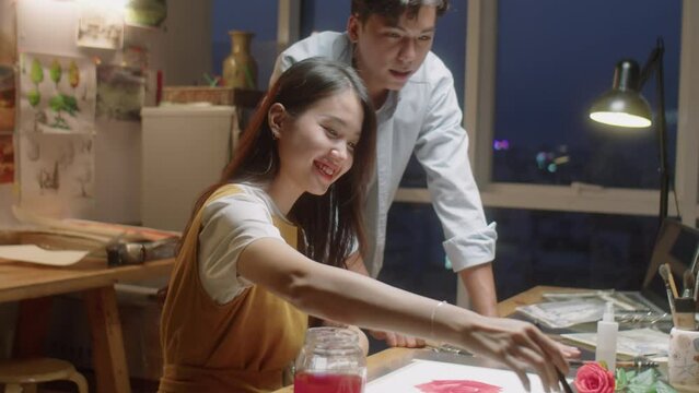 Medium shot of Asian teacher explaining female student how to paint picture while giving art class in studio