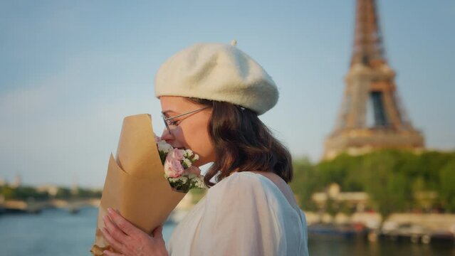 Happy girl smelling flowers in front of the Eiffel Tower on the bridge
