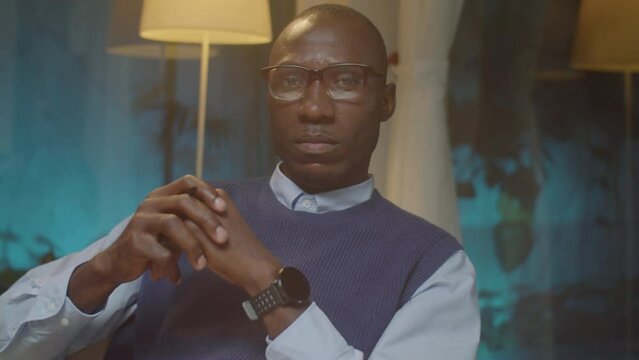 Portrait of serious African American psychologist posing for camera while sitting in his office in evening