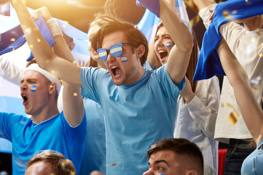 Sport fans with flags and paintings on faces, emotionally cheering up favourite football, soccer team of greece at stadium during game. Concept of sport, leisure time, emotions, hobby, entertainment