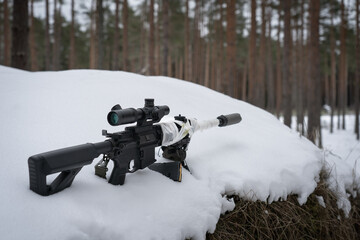 Sniper rifle with an optical sight and a silencer in the winter in the forest.
