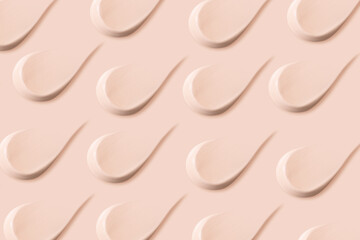Many identical strokes of foundation on a beige background. Light color.