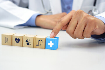 Finger of doctor touching the blue wooden block cube with healthcare medical icon symbol. Medical and health concept.