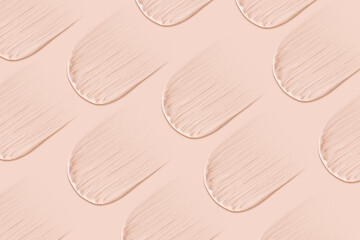 Many identical strokes of foundation on a beige background. Light color.