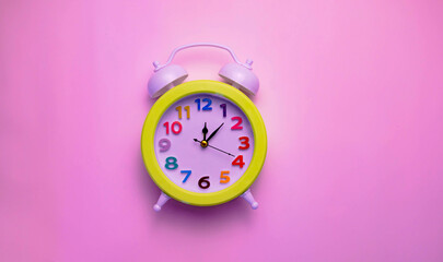 Bright alarm clock with a colored dial on a plain pink background.
