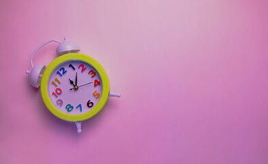 Bright alarm clock with a colored dial on a plain pink background.