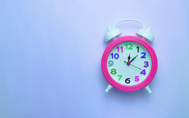 Bright pink alarm clock with a colored dial on a plain blue background.