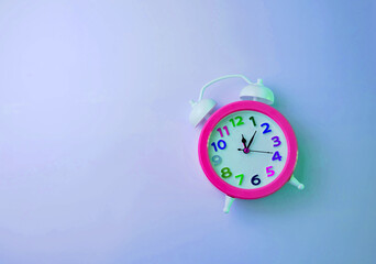 Bright pink alarm clock with a colored dial on a plain blue background.