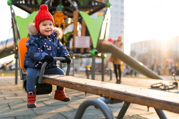 Happy beautiful little toddler girl having fun on swing in the playground. Baby smiles and laughing.