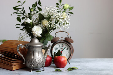 Vintage phone, rusty alarm clock, red apple gypsophila flowers on a desk. White background with copy space. Retro objects still life photo. 