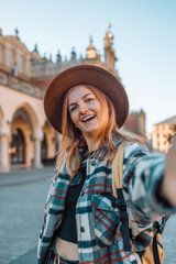 Portrait of 30s blonde woman with gorgeous smile with teeth and blonde hair taking selfie photo against old city center view in Krakow. High quality photo