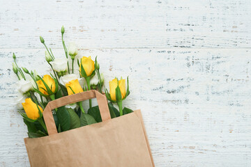 Easter concept. Bouquet of fresh white and yellow roses in paper bag on old white wooden...