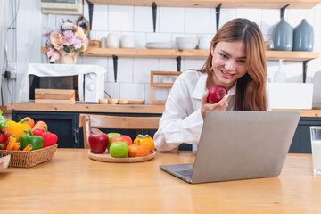 Obraz na płótnie Canvas Woman with a beautiful face in a white shirt is making a healthy breakfast with bread, vegetables, fruit and milk inside the kitchen and opening her laptop for cooking lessons. healthy cooking ideas.