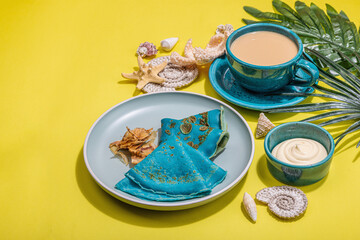 A cup of coffee and blue thin pancakes in a marine style. Starfish, sea shells, palm leaves