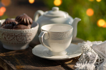 Obraz na płótnie Canvas Elegant cup, lace tablecloth, teapot, marshmallow in chocolate, wooden table. Outdoor breakfast, picnic, brunch, spring mood. Soft focus