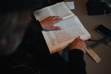 Naklejka premium Eine Person blättert durch ein religiöses Buch mit hebräischen Schriftzeichen und nutzt einen Zeiger für die Lesung