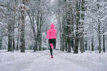 Running woman, girl runner on snow in park in winter sunny day.