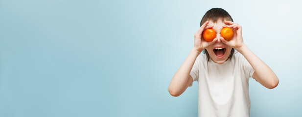 happy smiling boy with two mandarins covering his eyes on blue background.