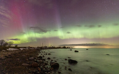 Scenic coastline and silky-smooth long shutter water reflecting the intense Northern lights in the sky