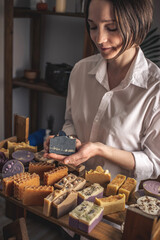 Female soap maker holds a handmade charcoal soap in her hands. A lot of different sliced pieces. Eco-friendly natural craft cosmetics