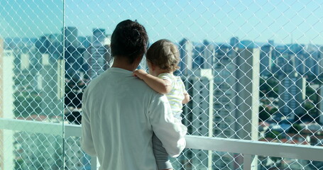Mother holding baby in arm looking at metropolitan city view. Mom and infant in apartment balcony with safety net
