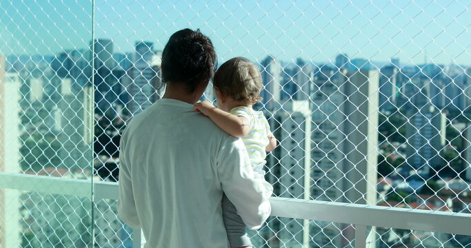 Mother holding baby in arm looking at metropolitan city view. Mom and infant in apartment balcony with safety net