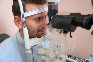 Calm Caucasian man is receiving qualified eyesight test in optician cabinet