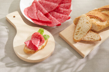 slice of salami with bread on a cutting board. sandwich with sausage and herbs. snack on a light table. meat delicacy under sunlight. antipasto close up. High quality 4k footage