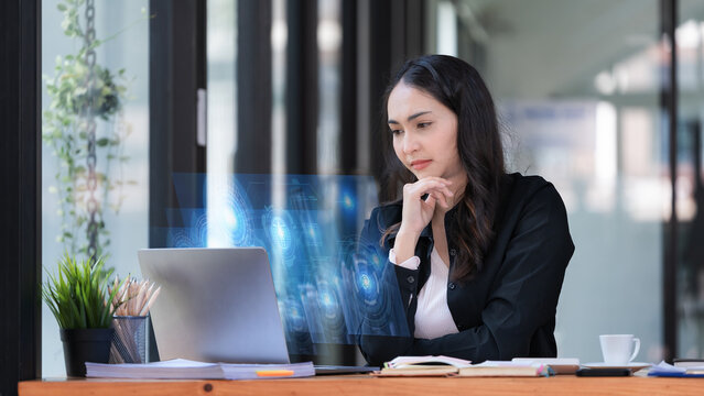 Portrait of an Asian businesswoman in a casual suit using a technology laptop for working via futuristic screen hologram in a modern office, Business owner and entrepreneur concept. - Powered by Adobe