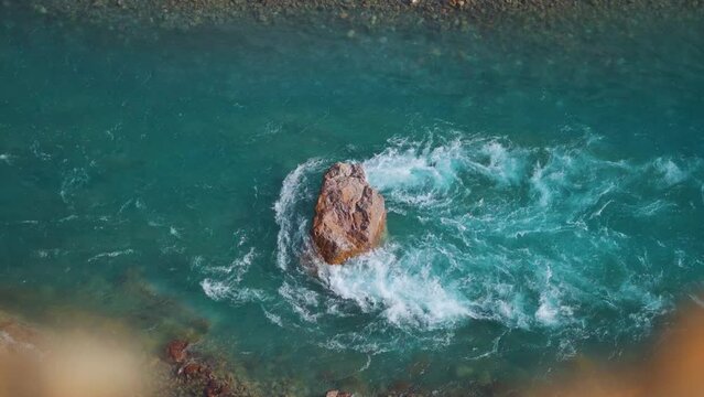 4K high angle shot of big rock in the middle of the blue water of the Tsarap Chu river flowing in between mountains as seen during the trek to the Phugtal Monastery in Zanskar, Ladakh, India.