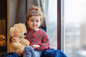 little cute girl with teddy bear sitting near window and smiling. child playing with soft toy. concept childhood