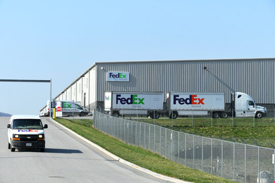 FedEx delivery vans and trucks driving out of a distribution center