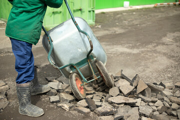 Builder removes broken stone. Man carries cobblestones in cart.