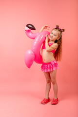 Happy joyful child girl in swimsuit having fun with swimming ring flamingo on a colored pink background. Summer beach concept