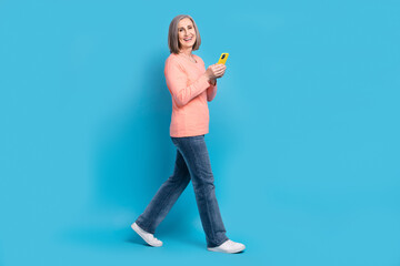 Full length cadre of excited old business lady walk steps hold smartphone browsing sliding shopping web site online isolated on blue color background