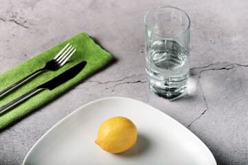 lemon on a white plate, a glass of water, a knife and a fork, the concept of a healthy diet for weight loss