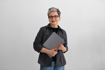An adult woman programmer in black clothes smiles on a gray background, holding a laptop in her...