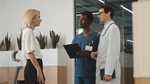 Elegant Caucasian blonde woman talking to her doctor and his nursing assistant after having medical checkup at modern clinic