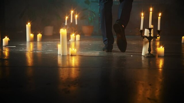 men's legs walking close-up in dark room many burning candles flame light on floor. Gothic guy prince vampire steps. black business suit classic shoes. Man king dark silhouette back body face cropped