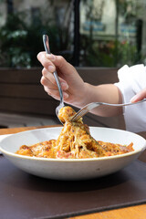 Manos levantando pasta con salsa de camarones y queso fundido,