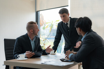 Group of diverse businessman going over paperwork together and working on laptop at meeting.