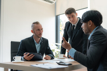 Group of diverse businessman going over paperwork together and working on laptop at meeting.